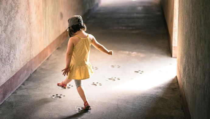 A young girl walking down a sandy corridor leaving behind footprints.
