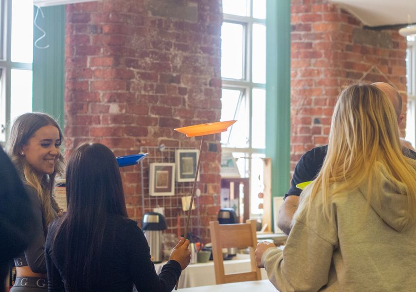 School children laughing in a red brick room whilst spinning plates on a stick.