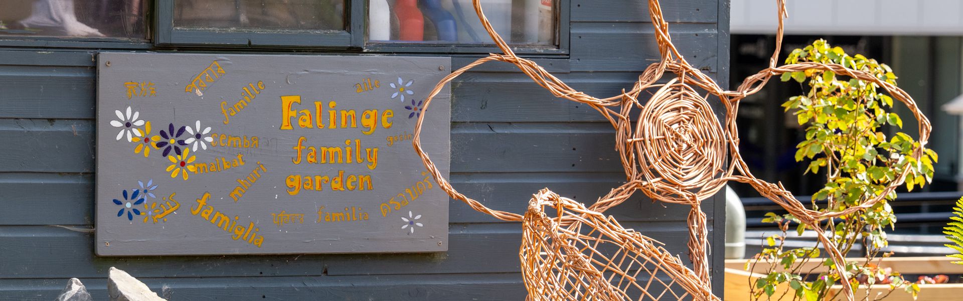 A sign on a shed that says "Falinge Family Garden" next to planters with dirt and small plants ready to grow.