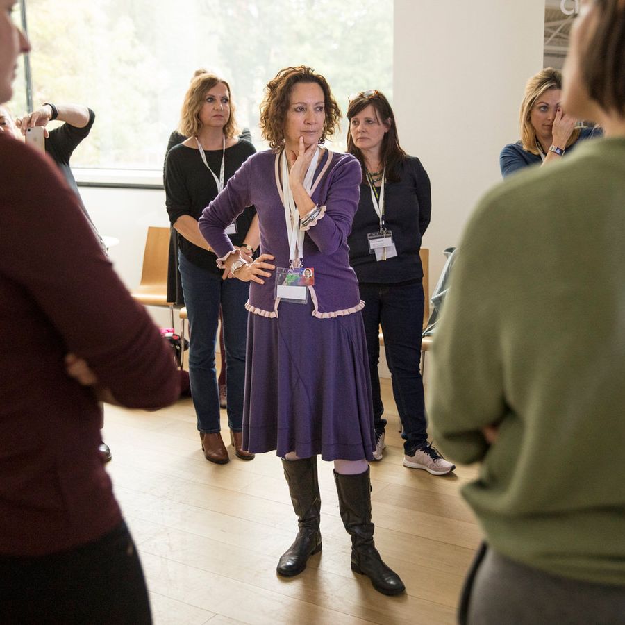 Jude is pictured, standing in the centre of a group of people at a Curious Minds Schools Arts Festival in 2019. She is deep in tought, wearing her favourite colour - purple.