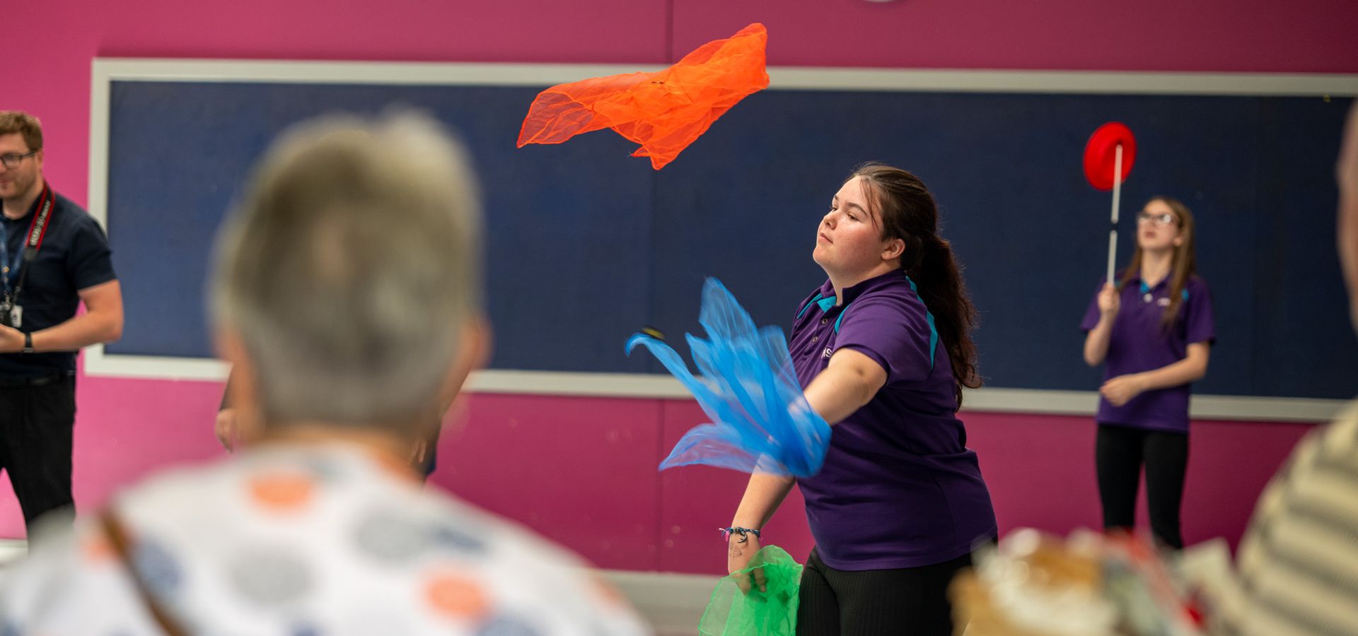 Two pupils in Falinge Park High School uniform practice their circus skills. One is juggling colourful fabrics, the other is spinning plates.