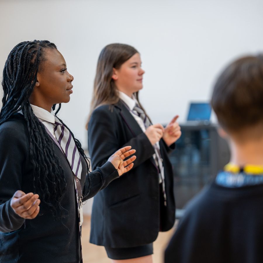 A young high school girl is stood with their hands out as part of a round circle game.