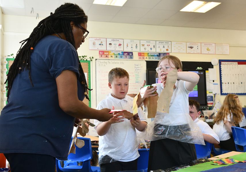 A teacher interacts with school pupils in a classroom. They are working on an art project