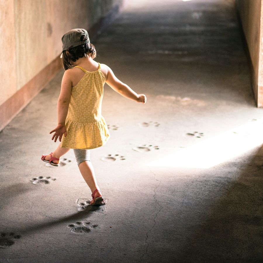 A young girl walking down a sandy corridor leaving behind footprints.