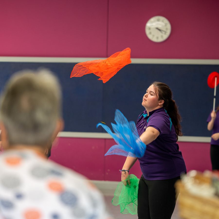 A young girl in a school uniform throwing and catching colourful pieces of paper.