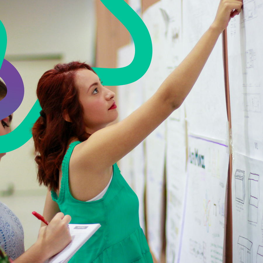 A woman pointing up at a wall full of  large pieces of paper with hand-written notes. 