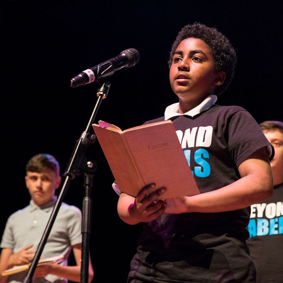 Young performers on stage in matching black t-shirts, stood in front of microphones.